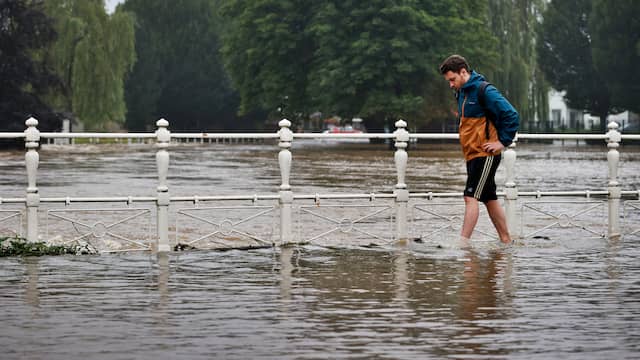 Een man waadt zich door de buiten de oevers getreden rivier de Geul.