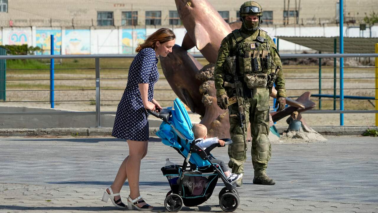 Жена минава покрай руски войник в Херсон с детето си.
