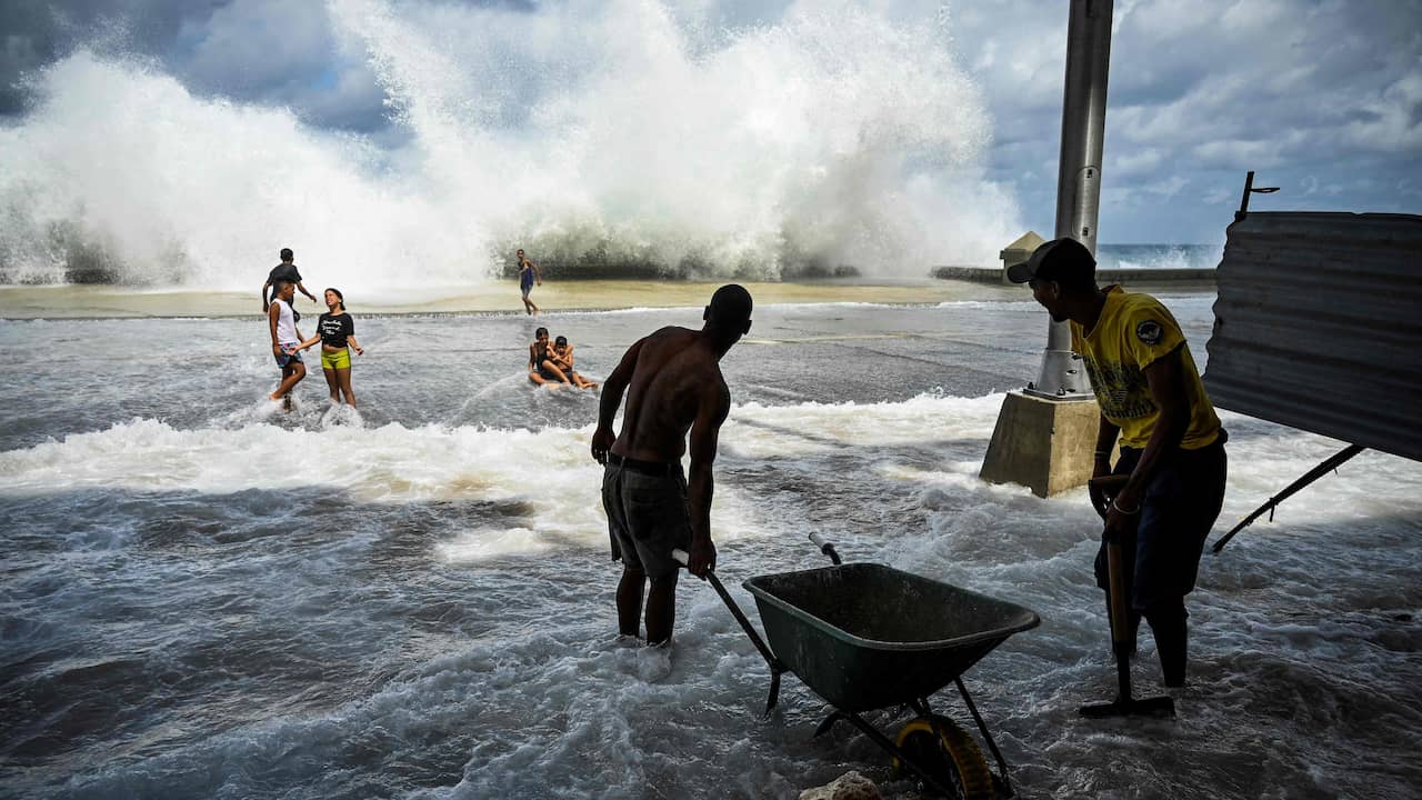 Ian ha causato molti danni anche nella parte occidentale di Cuba.  Qui, i lavoratori municipali riordinano il caos a L'Avana mentre osservano i bambini che giocano nell'acqua.