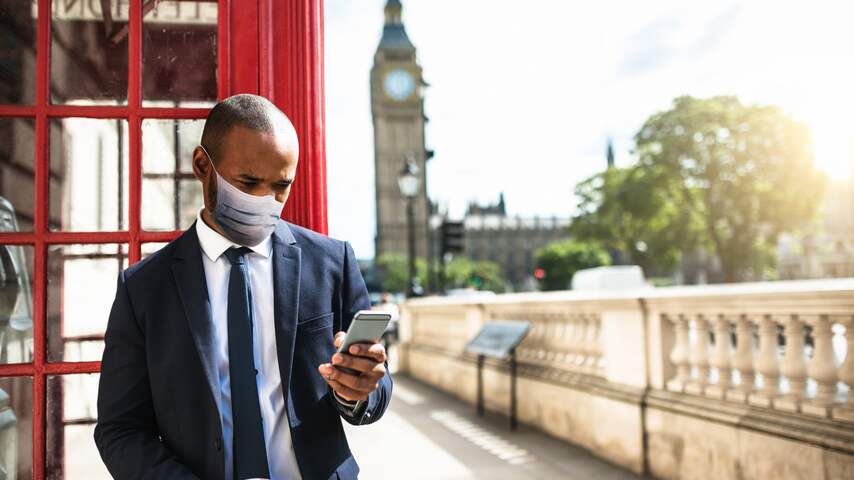 Man met smartphone en mondkapje vanwege coronavirus in Londen