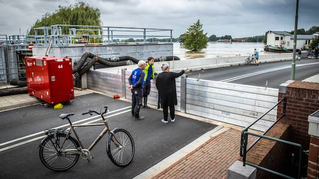 Mensen staan te kijken naar het hoge water bij een gesloten coupure waar de Roer in de Maas stroomt in het centrum van Roermond.