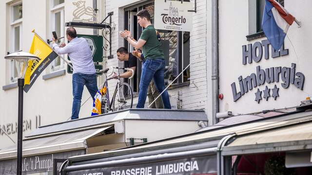 Drie wielerfans volgen de koers op een afdakje van een hotel in Valkenburg.