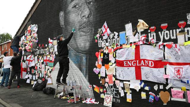 Een straatartiest repareert de muurschildering van Marcus Rashford.