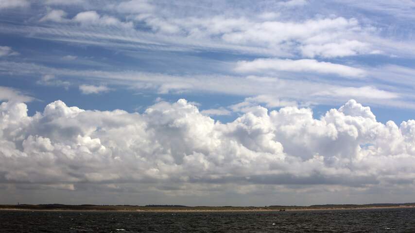 Helder blauwe lucht op zee, wolken boven land