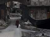 Een oudere Syrische vrouw steekt de straat over. Naast haar hangt een groot zwart doek, dat het gebied moet aangeven waar de gevechten plaatsvinden. Momenteel wordt er onderhandeld over een staakt het vuren.