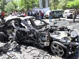 Mensen verzamelen zich op de plaats van een explosie in de wijk Mazzeh van de Syrische hoofdstad Damascus. Een auto is volledig afgebrand. 