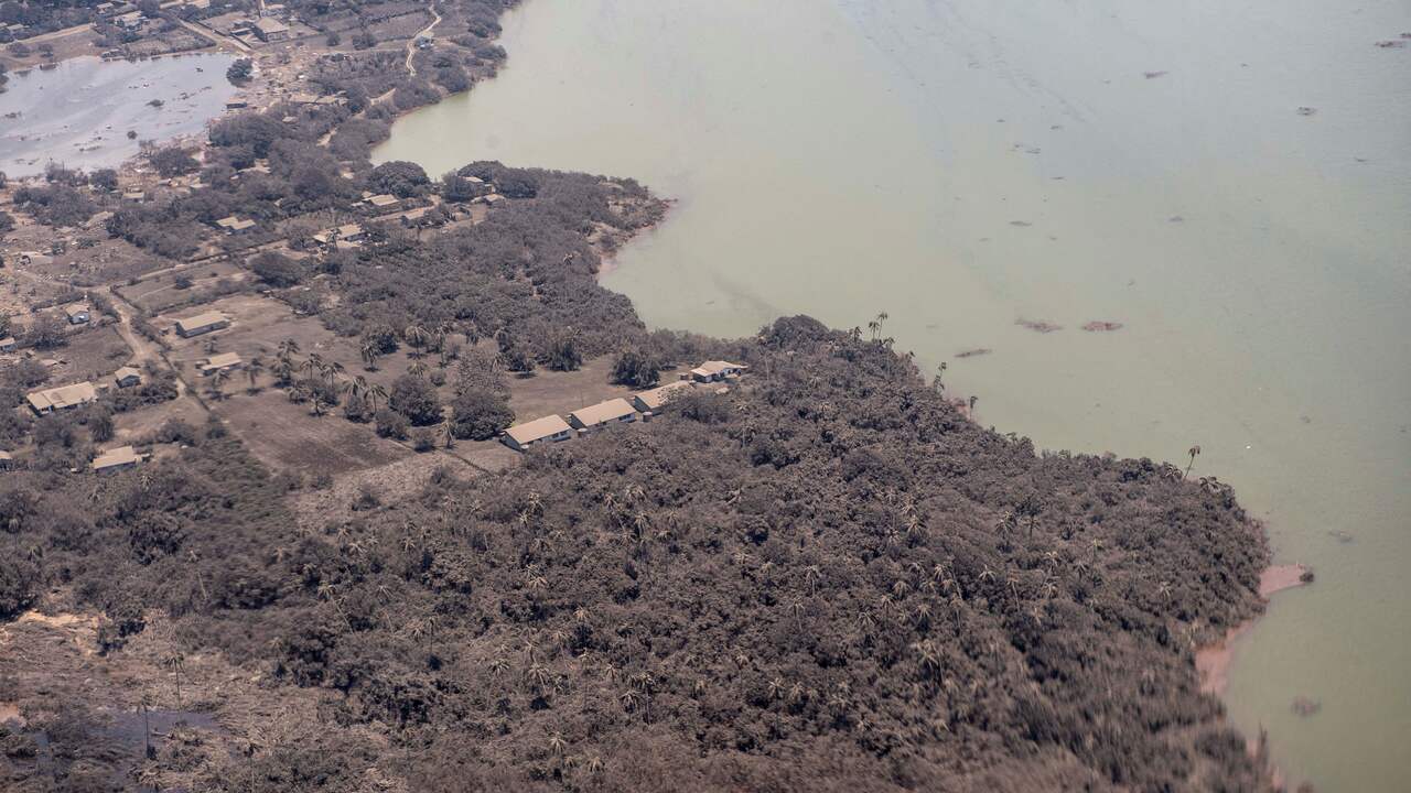 Een foto van een Nieuw-Zeelandse defensiehelikopter. Het landschap en de huizen op Tonga zijn volledig bedekt met vulkaanas.