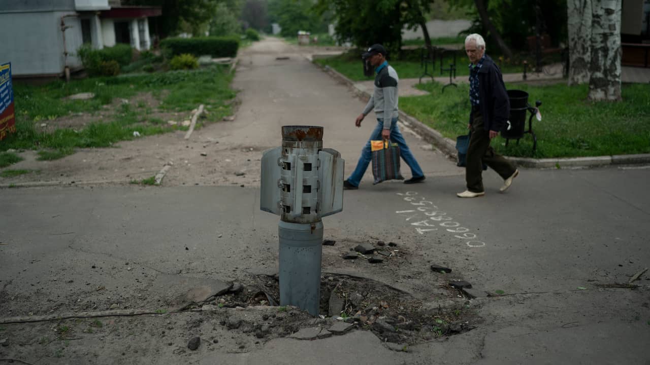 Mensen lopen langs een raket die zich in het wegdek heeft geboord in het Oost-Oekraïense Luhansk.
