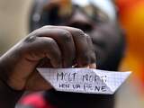 Een asielzoeker heeft een papieren boot in zijn hand waarop in het Italiaans 'Te veel doden, dat is niet goed' staat geschreven.